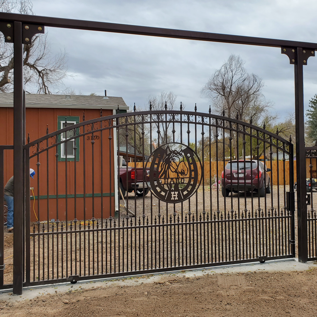 Arched wrought iron entry gate with custom scrollwork, vehicles parked beyond