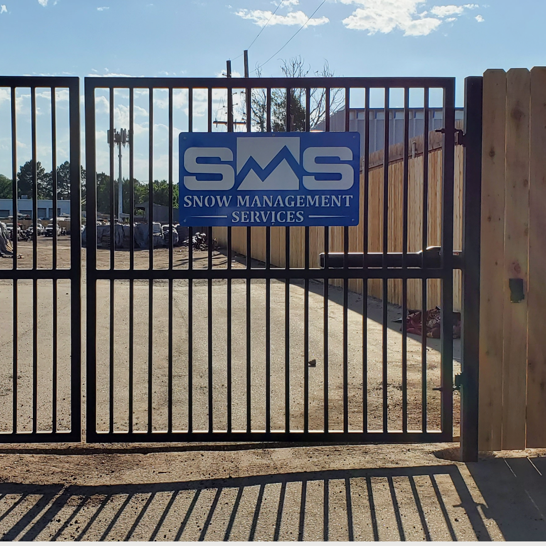Large steel slat security gate between posts at a commercial yard entrance