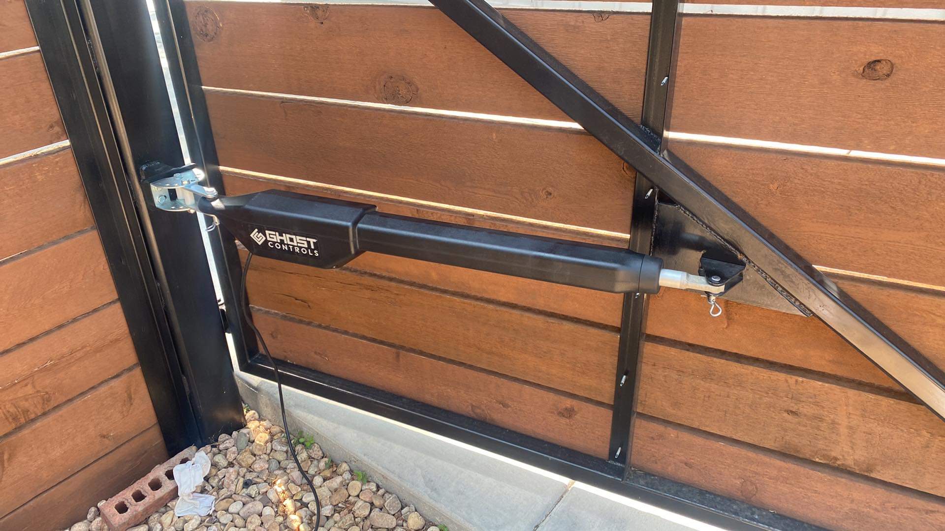 Close-up of an automatic gate opener mounted on a gate with wood and steel posts